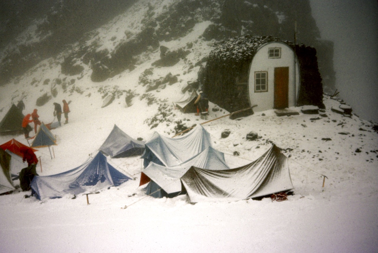 Fresh snow covers mountaineering tents and a stone shelter at Camp Schurman on Mt Rainier