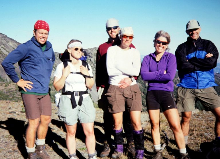 Six hikers in colorful clothing stand at Augusta Pass in the Chiwaukum Mountains