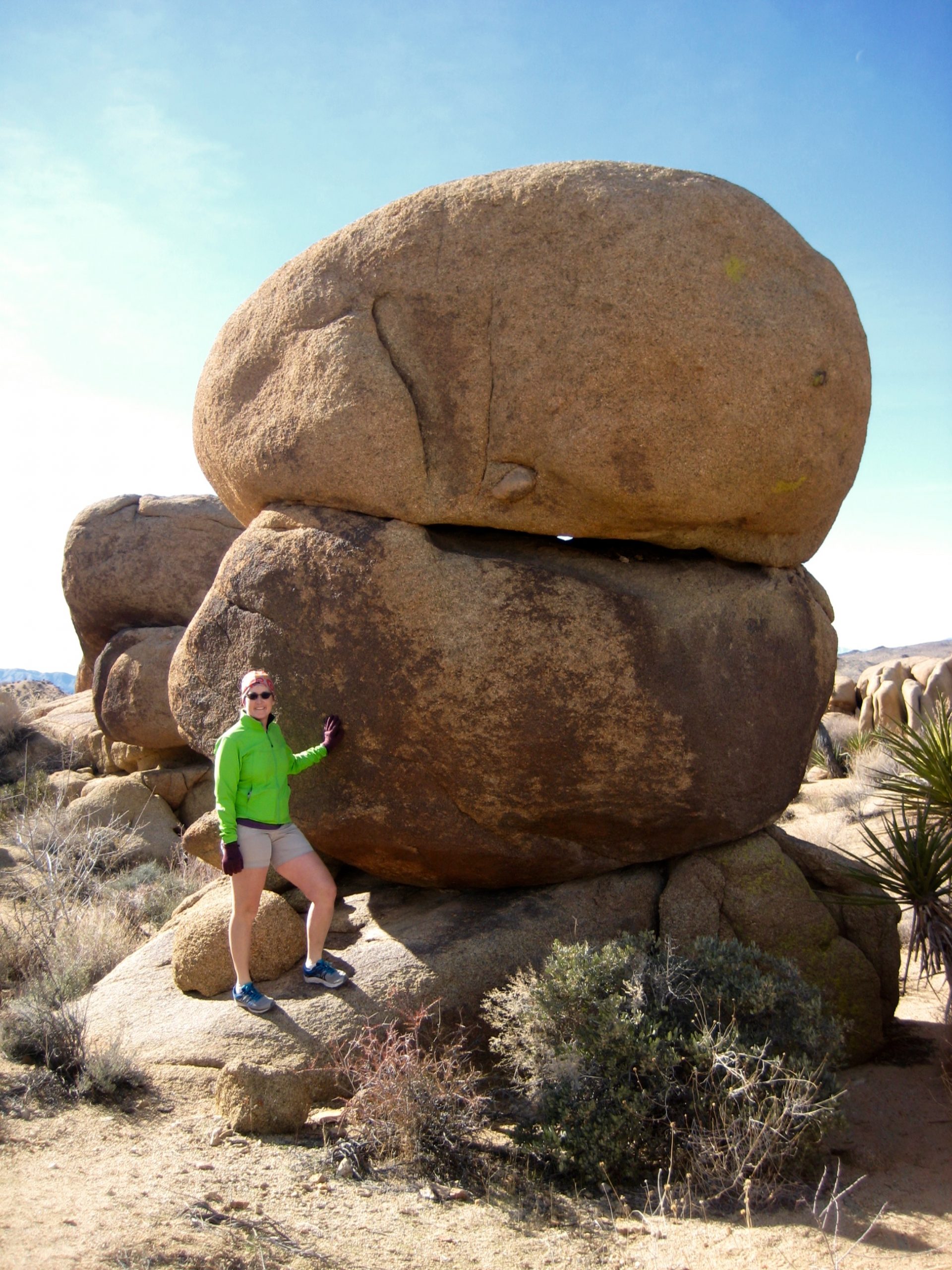 hiker standing next to stacked giant boulder in the dessert sand along the Mastodon hiking loop in Joshua Tree National Park