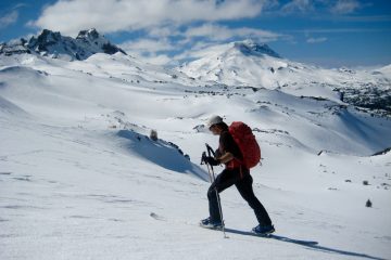 A backcountry skier glides along the top of Tam McArthur Rim in the Deschutes Mountains of Oregon with Broken Top & South Sister in the background