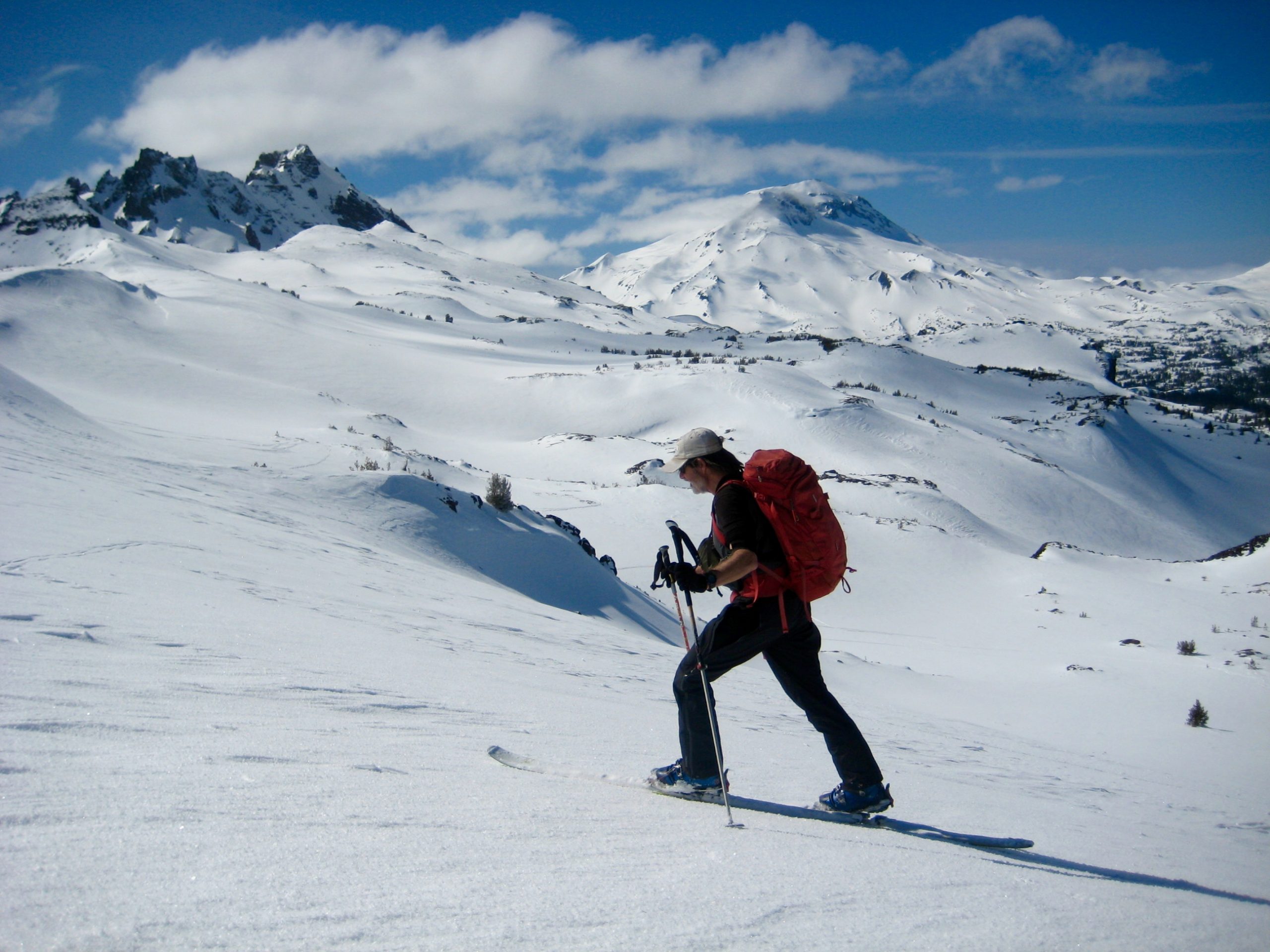 A backcountry skier glides along the top of Tam McArthur Rim in the Deschutes Mountains of Oregon with Broken Top & South Sister in the background