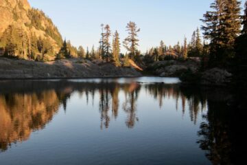 Orange alpenglow reflects off a glassy lake in the Alpine Lakes Wilderness, Washington