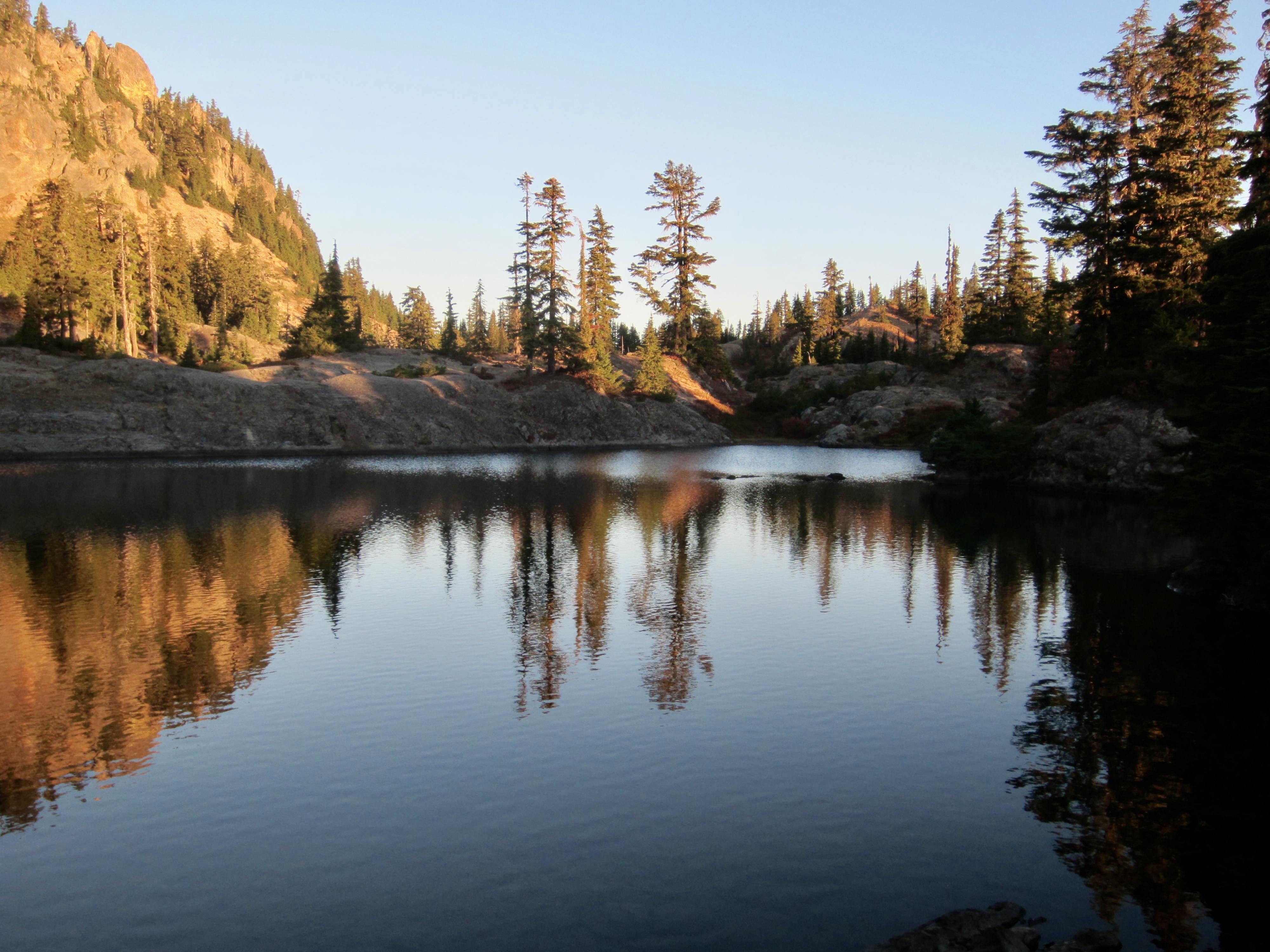 Orange alpenglow reflects off a glassy lake in the Alpine Lakes Wilderness, Washington