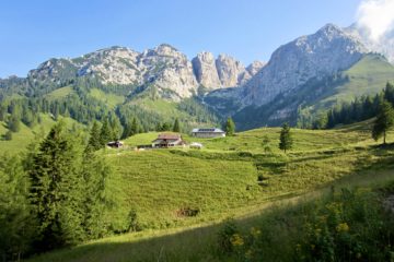 A rifugio sits in a grassy meadow with rugged mountains behind in the Italian Dolomites