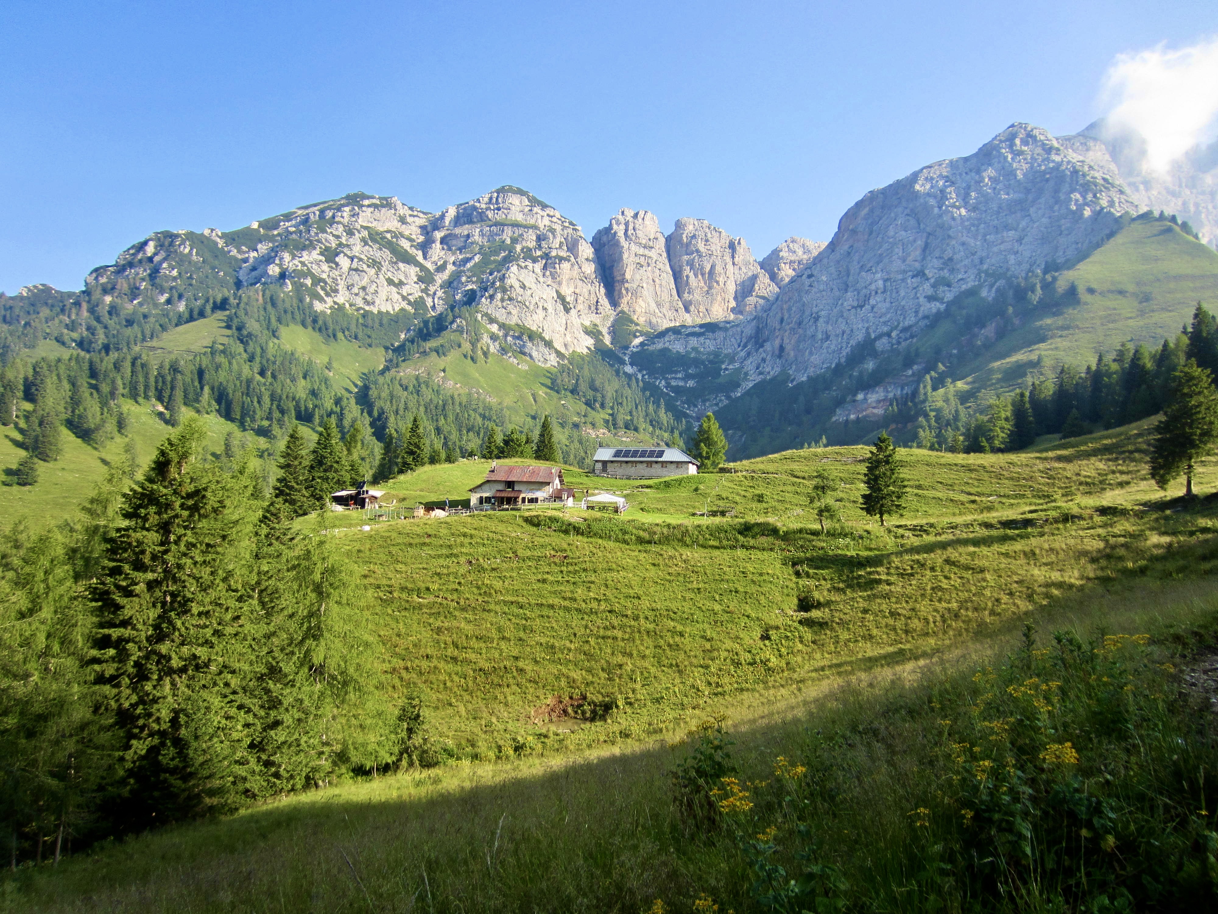A rifugio sits in a grassy meadow with rugged mountains behind in the Italian Dolomites
