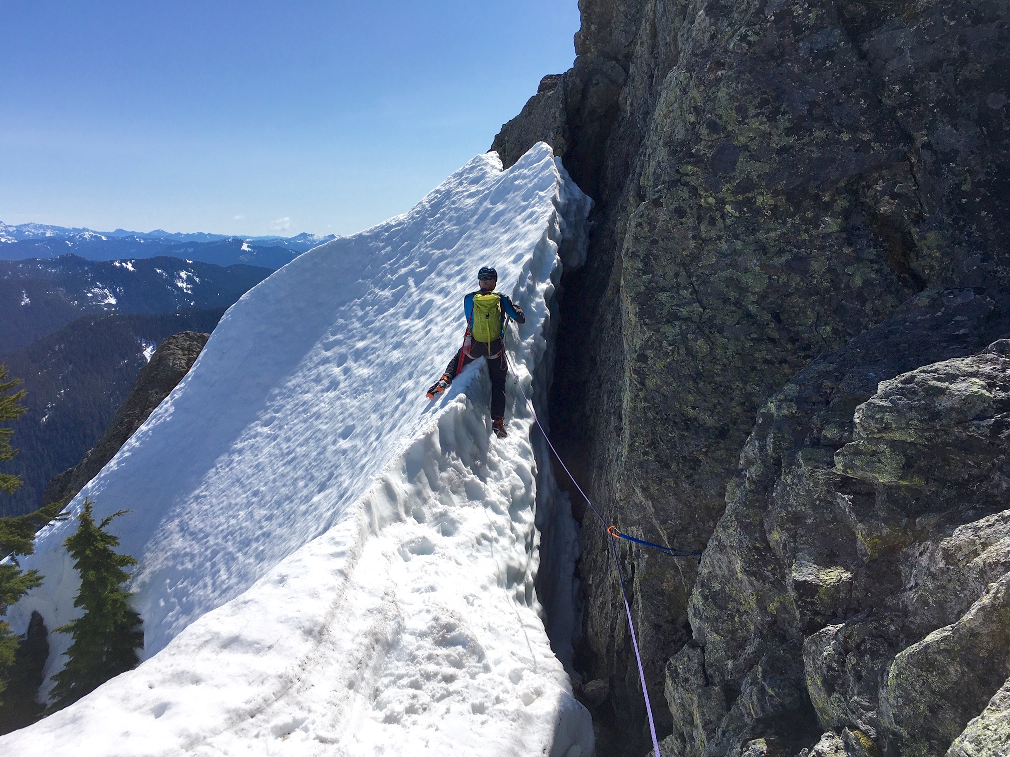A mountain climber crosses a steep snow finger closely below the summit of Wing Peak in the Skykomish Mountains