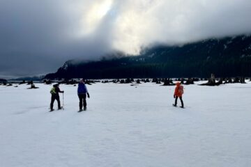 Three snowshoers walk across drawdown flats of Keechelus Lake, WA