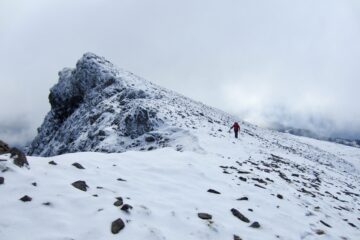 A lone hiker moves along the snowy summit ridge of Mt. Outram in the Canadian Cascades.