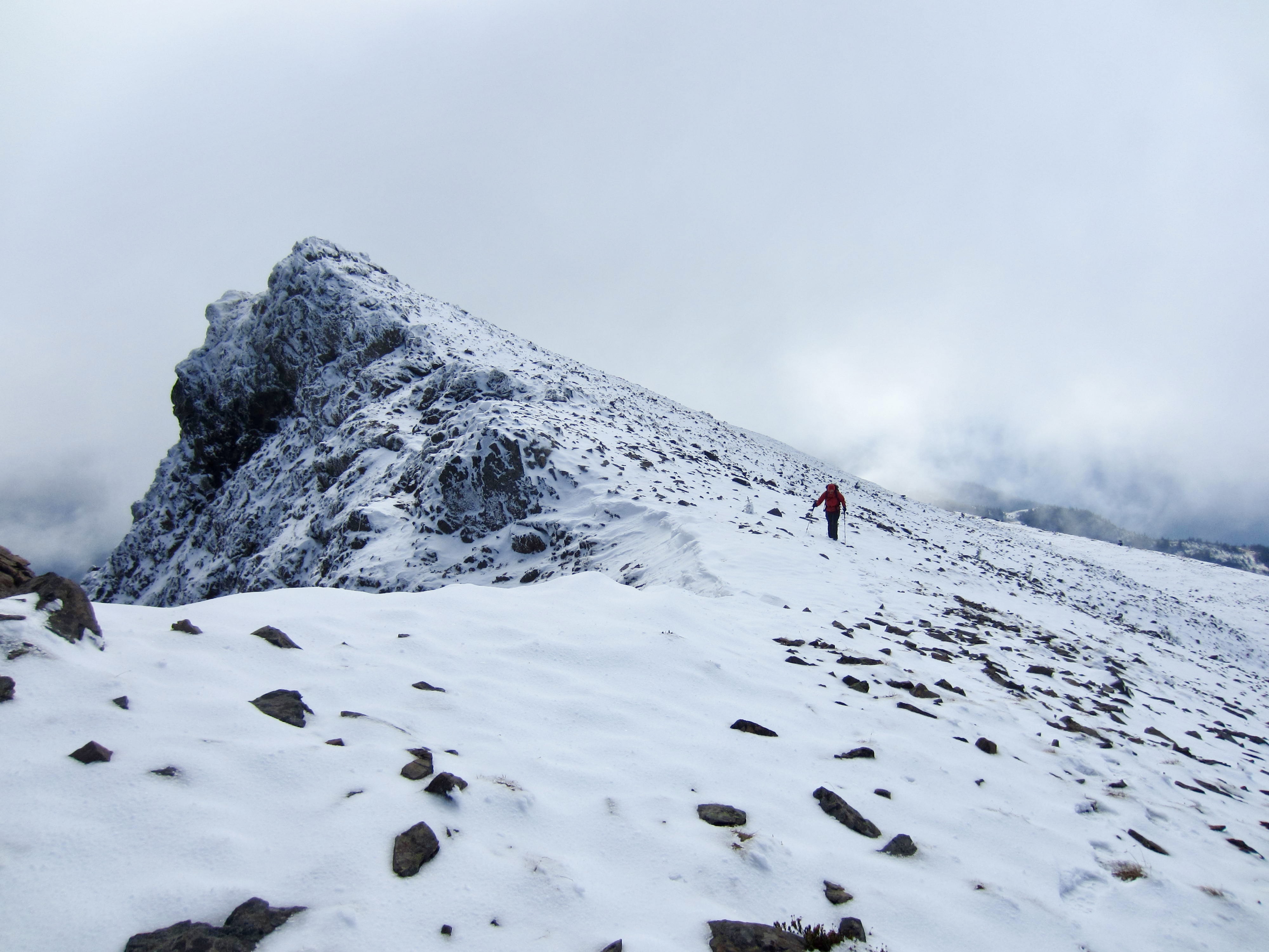 A lone hiker moves along the snowy summit ridge of Mt. Outram in the Canadian Cascades.