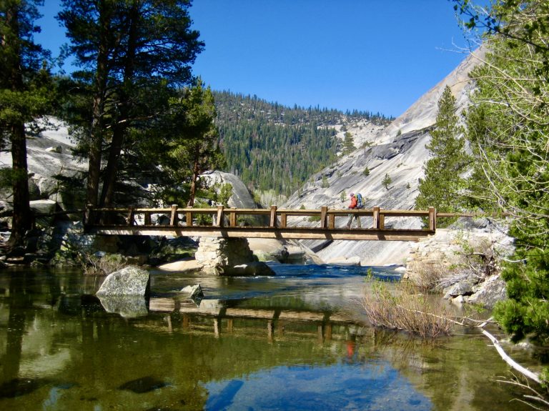 A backpacker crosses a bridge over the Merced River in Upper Merced Canyon of Yosemite National Park