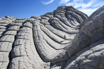 A lone explorer walks up a tessellated sandstone swale at White Pocket in Vermilion Cliffs National Monument, Arizona