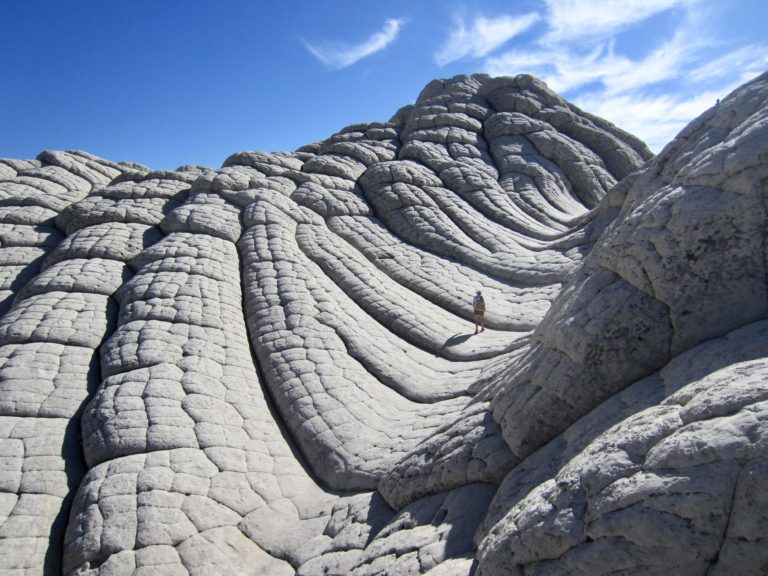 A lone explorer walks up a tessellated sandstone swale at White Pocket in Vermilion Cliffs National Monument, Arizona
