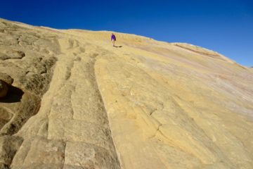 A lone hiker ascends a multi-colored slab of sandstone on Yellow Rock in Grand Staircase - Escalante National Monument, Utah
