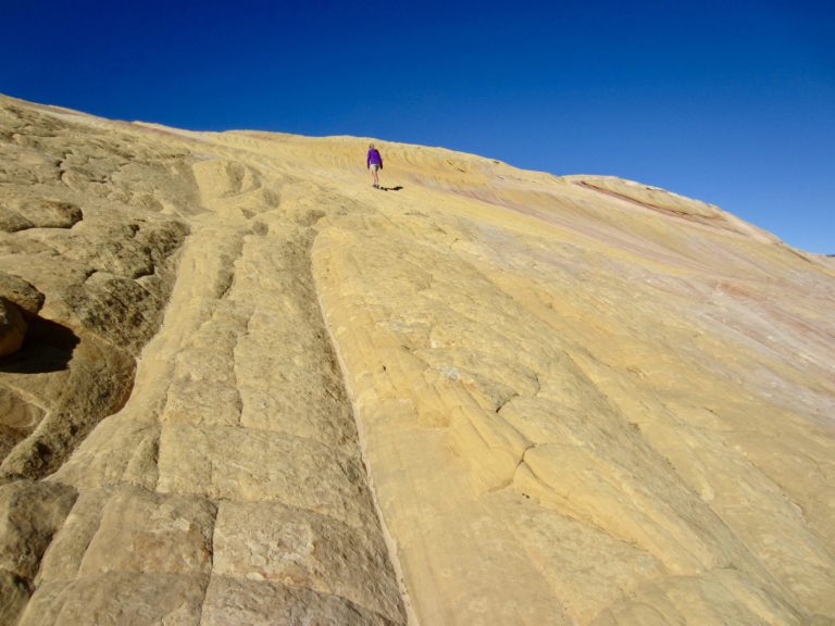 A lone hiker ascends a multi-colored slab of sandstone on Yellow Rock in Grand Staircase - Escalante National Monument, Utah