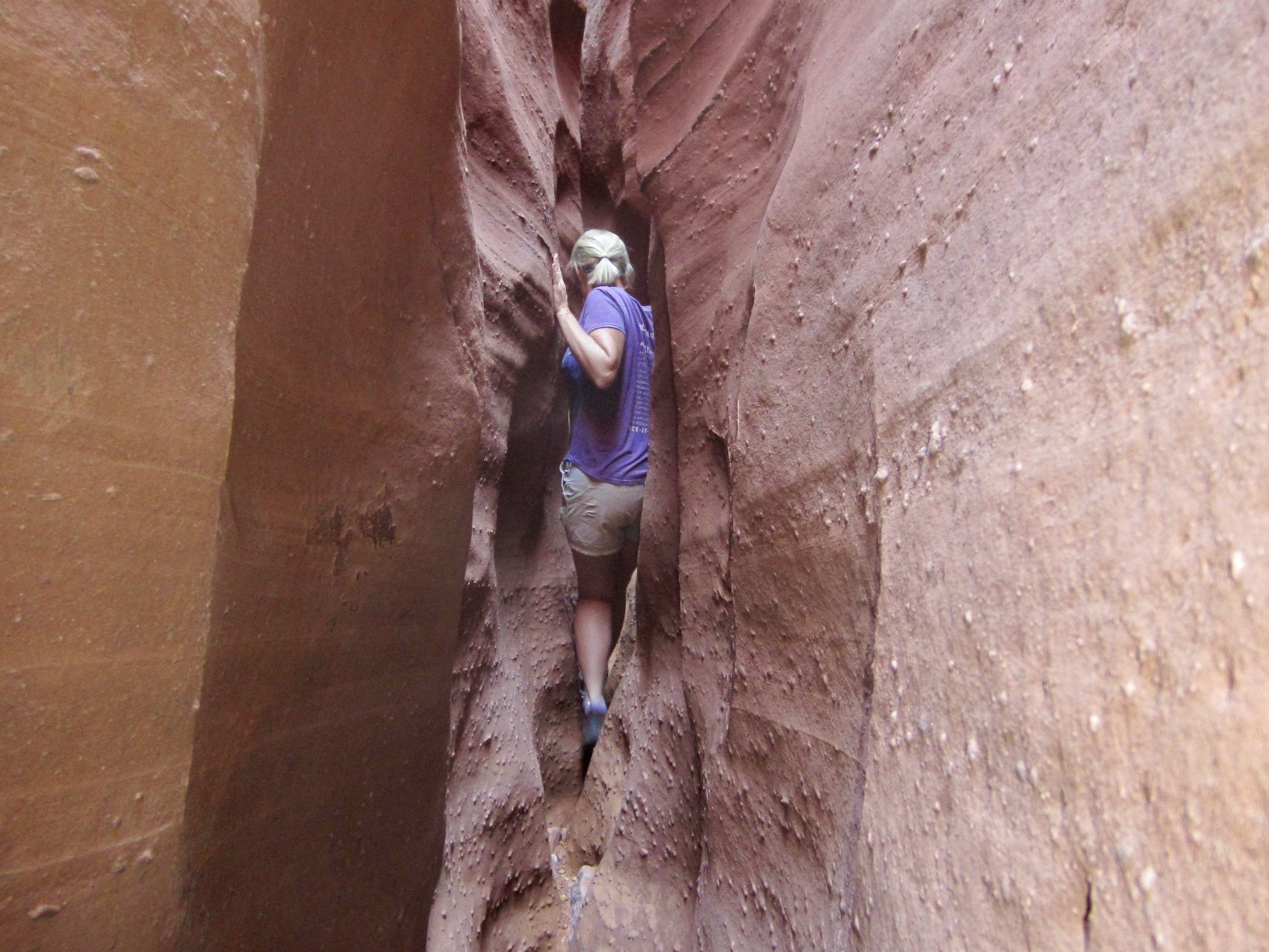 A woman squeezes thru a narrow gap in Spooky Slot Canyon in the Dry Fork Coyote Gulch area of Utah